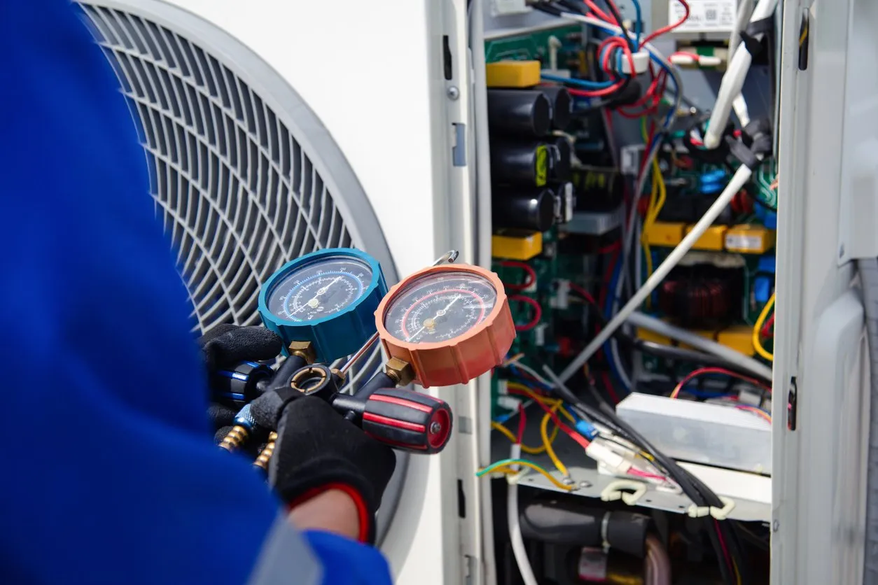 Certified technician using pressure gauges to service an outdoor air conditioning compressor unit